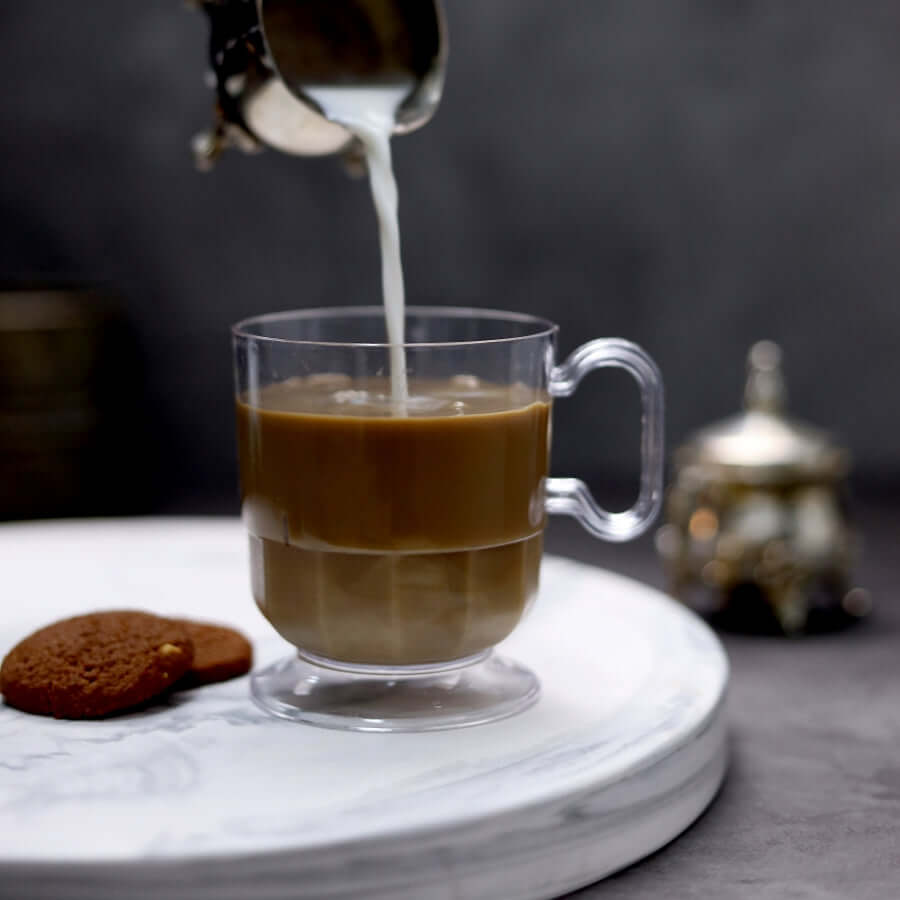 Clear glass coffee mug with milk being poured, accompanied by cookies.