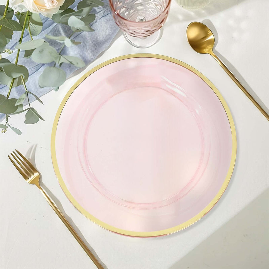 Pink plate with gold rim on a table setting with cutlery and greenery.