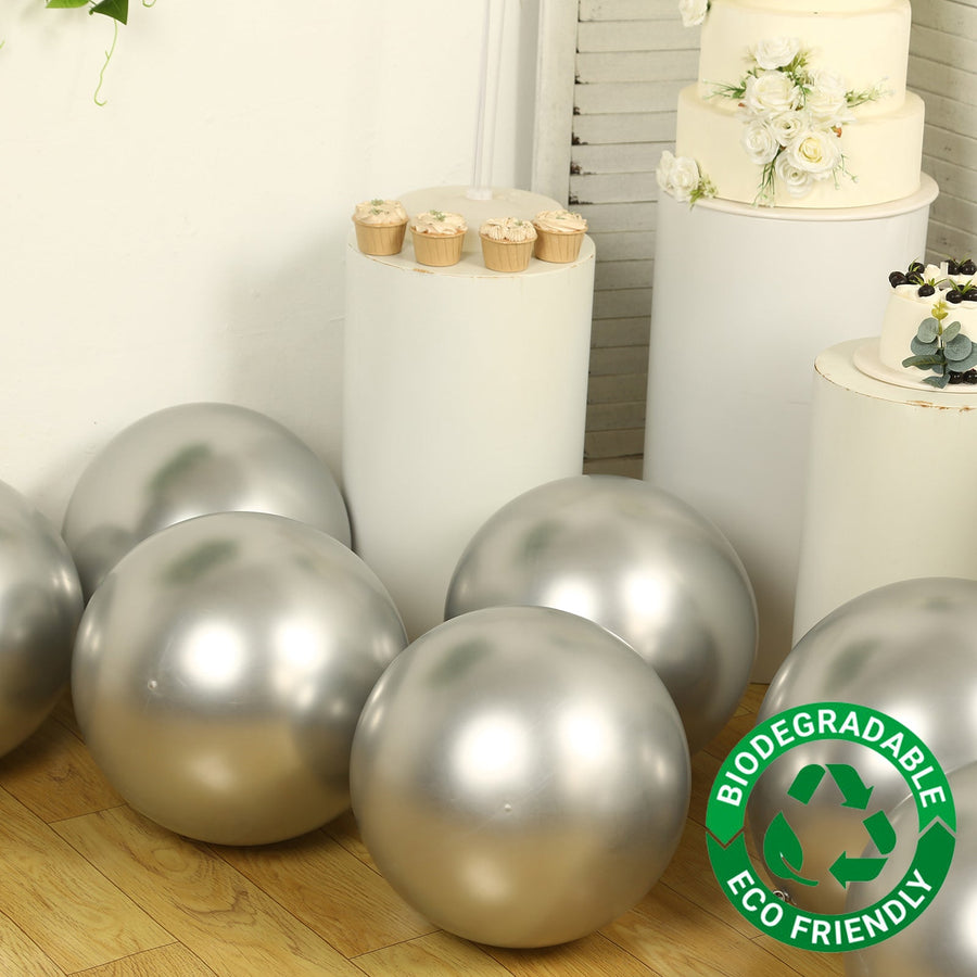 Silver biodegradable balloons arranged near a cake display in an event setting.