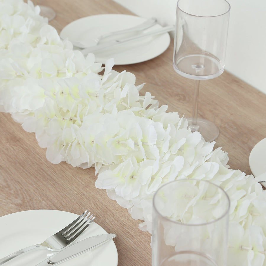 White floral table runner on a wooden table with plates and glassware.