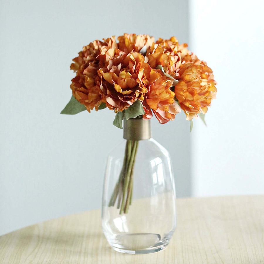 Orange flower bouquet in a clear glass vase on a wooden table.