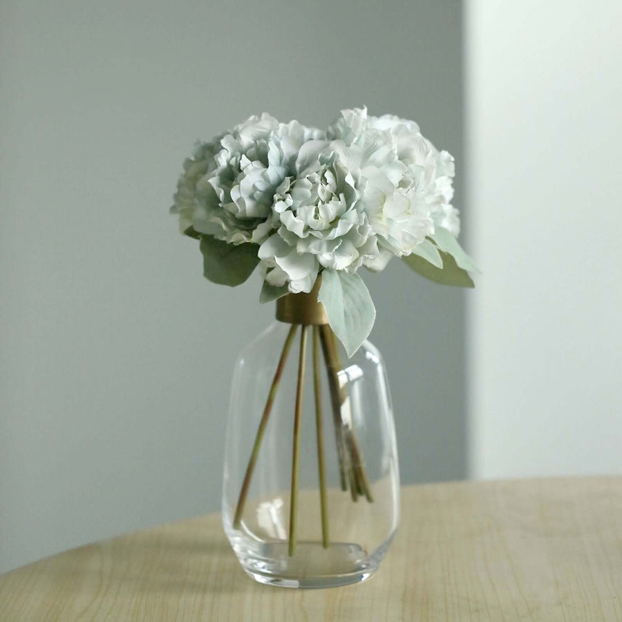 Artificial flower bouquet in a clear vase on a wooden table.