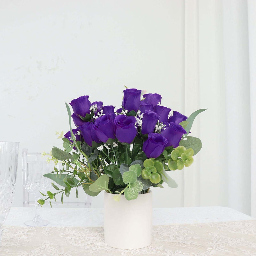 Purple rose bouquet in a white pot with greenery accents.
