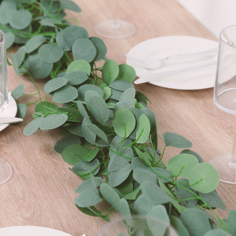 Artificial eucalyptus garland on a wooden table setting with plates and glasses.