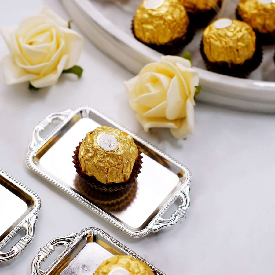 Gold-wrapped chocolate truffles on silver trays with white roses.