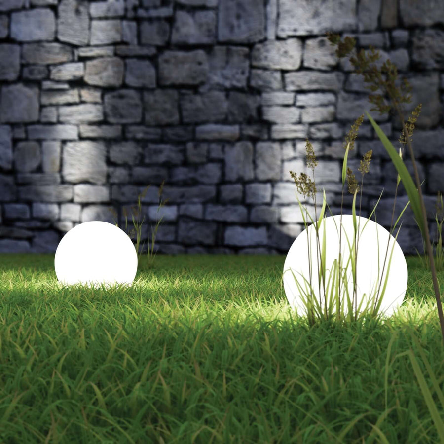 Illuminated garden spheres glowing on grass with a stone wall backdrop.