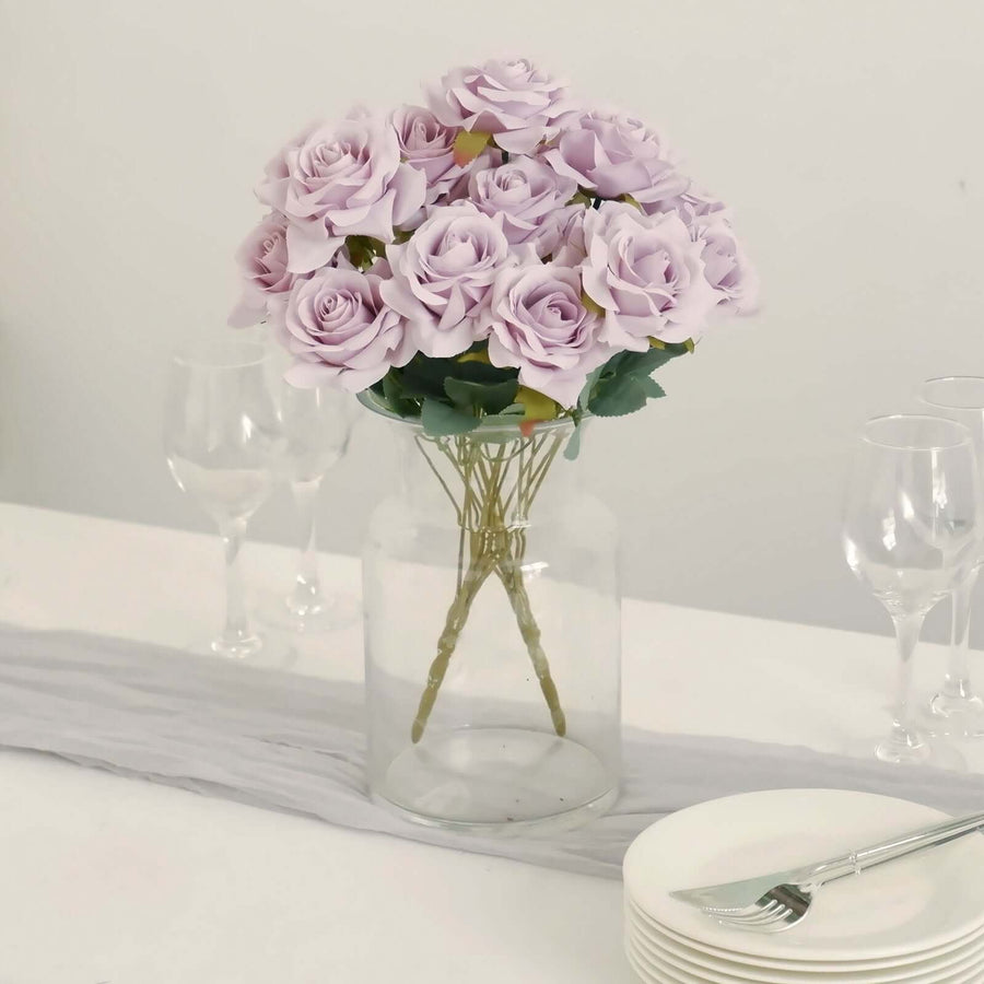 Purple faux roses in a clear vase on a dining table with dinnerware.