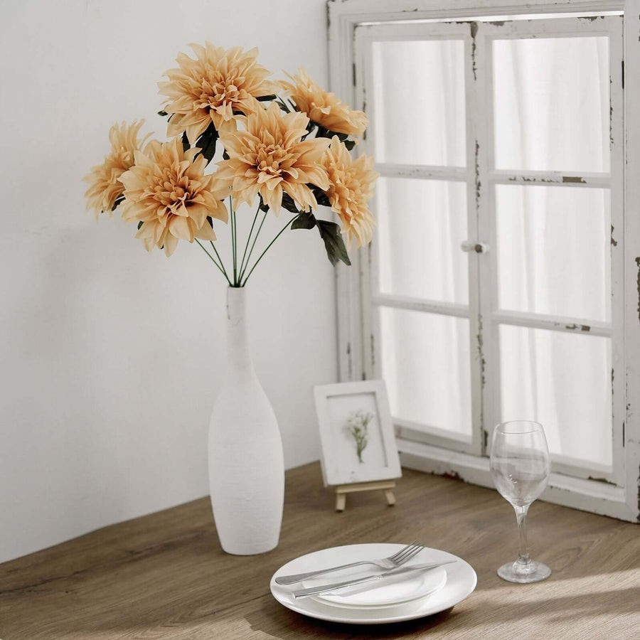 Artificial yellow flowers in a vase on a dining table with plates and glassware.