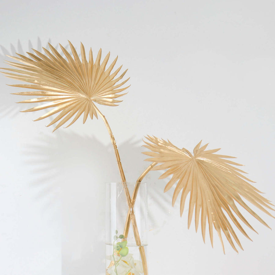 Gold decorative palm leaves in a clear vase.