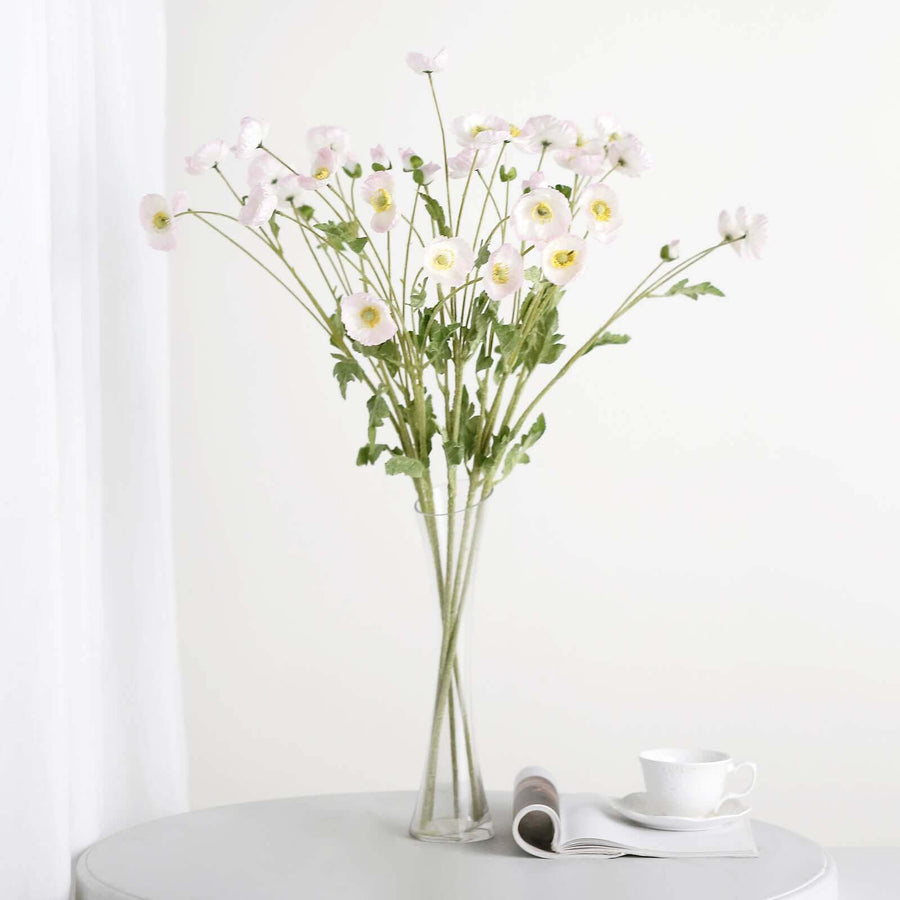 Pink flowers in a clear vase on a table with a cup and magazine.