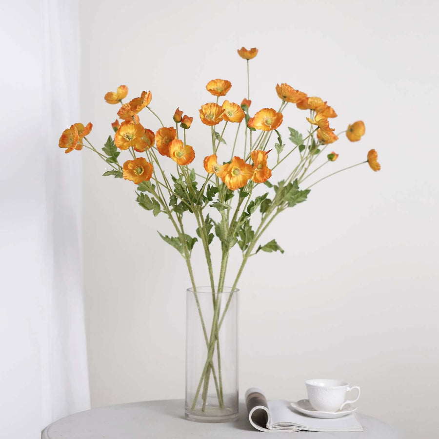 Vibrant orange ranunculus flowers in a clear vase on a table