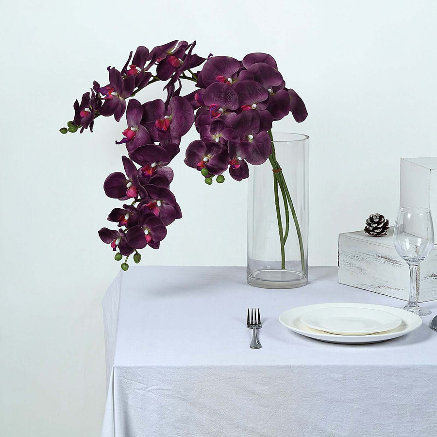 Purple orchid arrangement in a vase on a table setting.