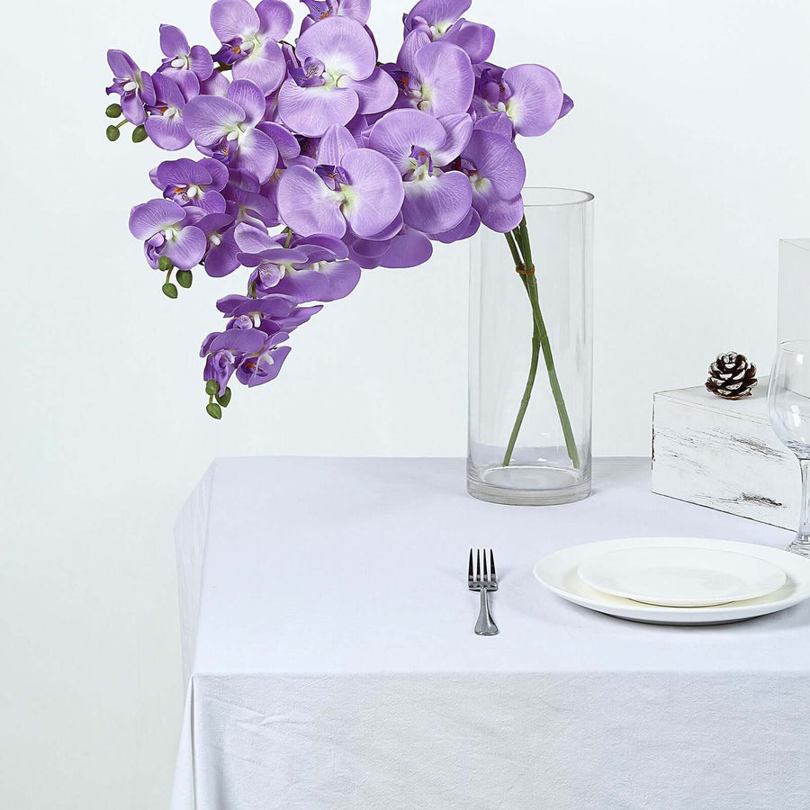 Purple orchid arrangement in a clear vase on a white tablecloth
