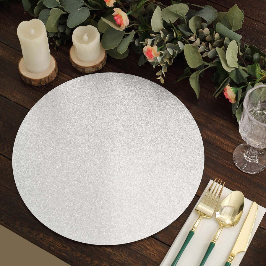 Silver round placemat on a rustic table with candles and greenery.