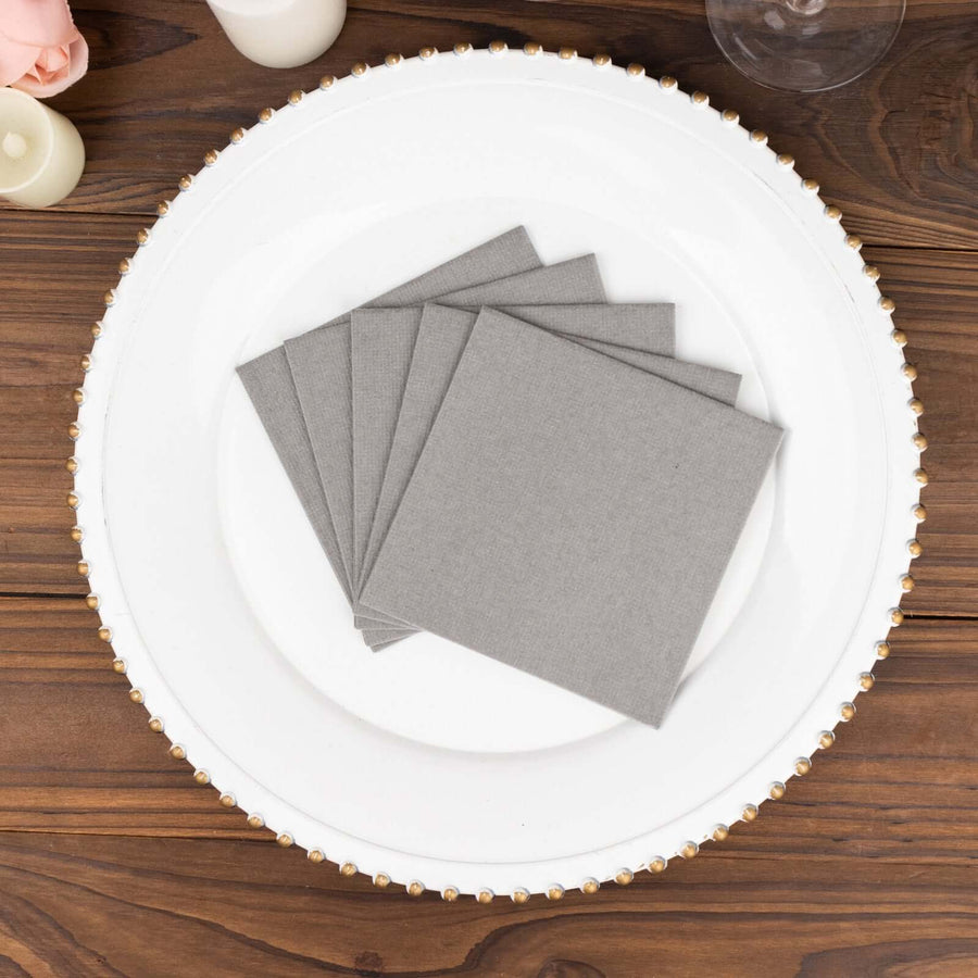 Gray cloth napkins arranged on a white plate on a wooden table.
