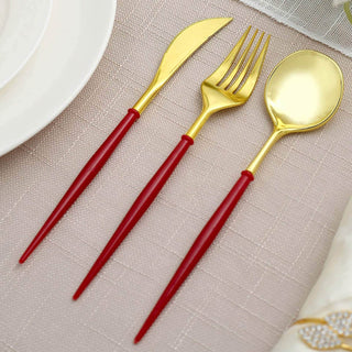 Gold cutlery set with red handles on a textured tablecloth.