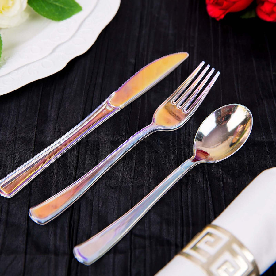 Set of elegant iridescent cutlery: knife, fork, and spoon on a black tablecloth.