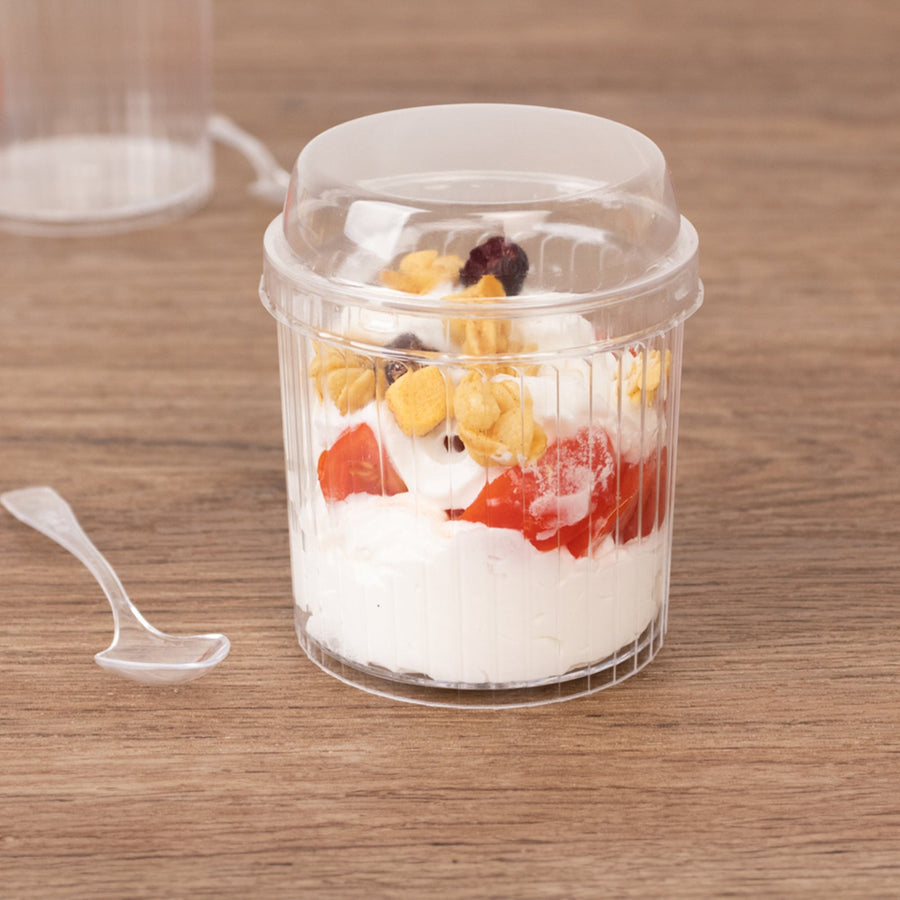 Plastic dessert cup with yogurt, strawberries, and granola on a wooden surface.