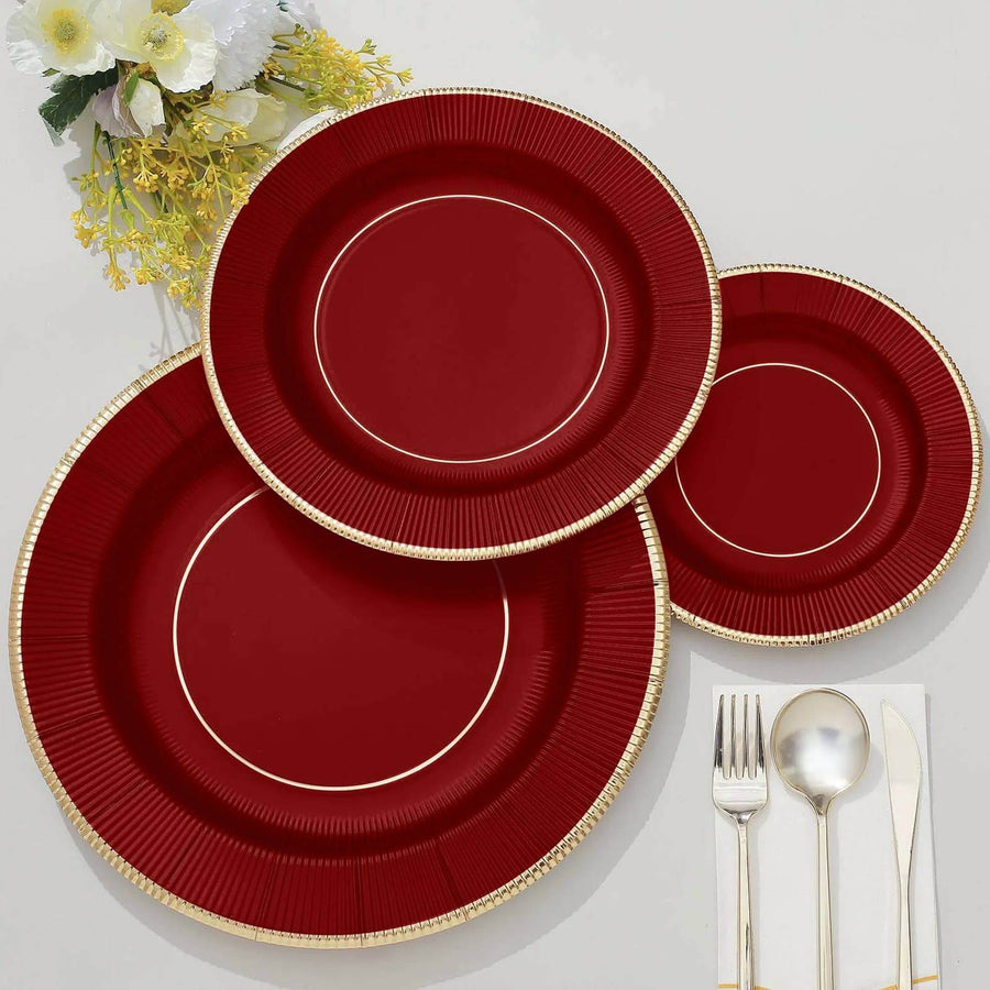 Elegant red disposable plates with gold rims on a neutral surface.