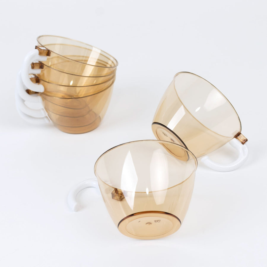 Set of transparent amber cups with white handles on a plain background
