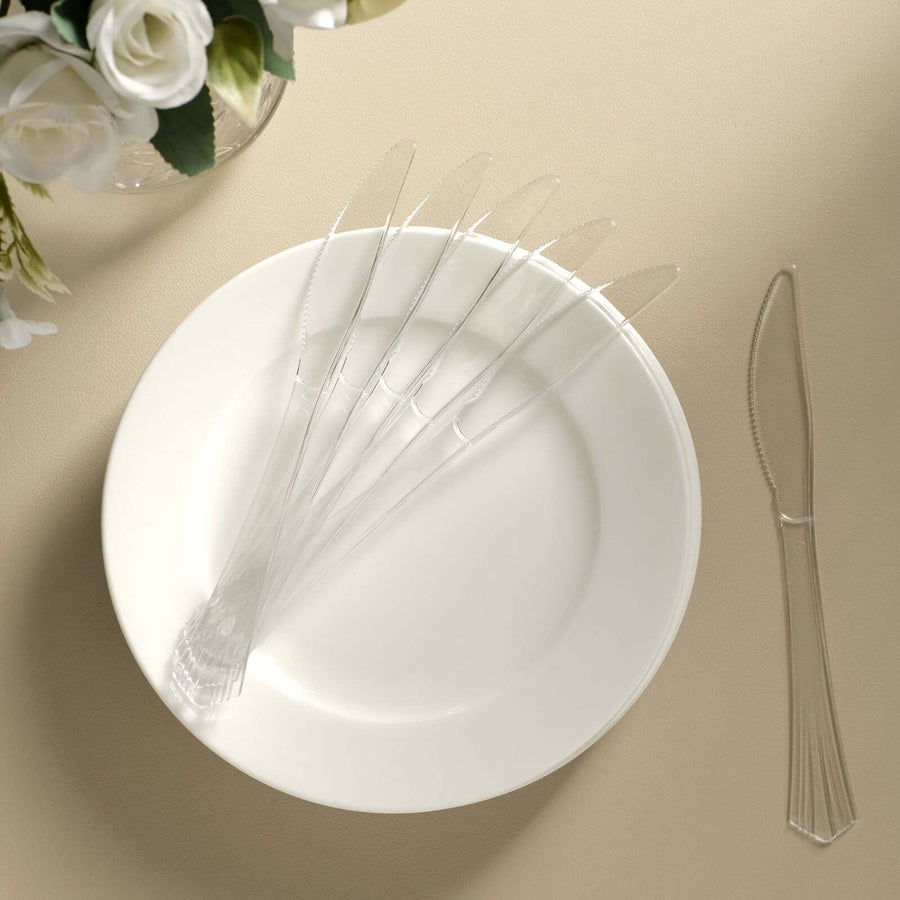 Clear plastic knives arranged on a white plate against a beige background.