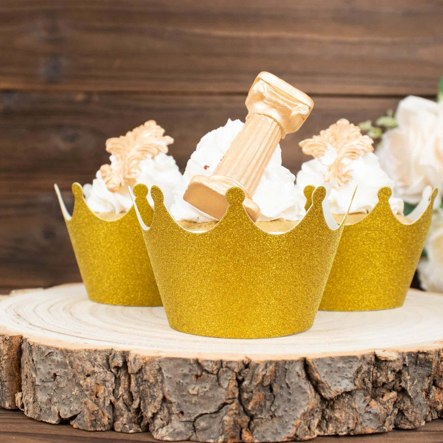 Gold crown cupcake wrappers with decorative toppers on a wooden slice.