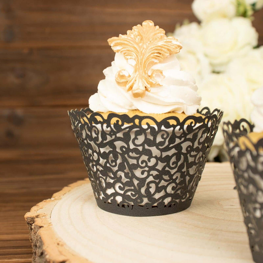 Black lace cupcake wrapper with gold decorative topper on a wooden slice.