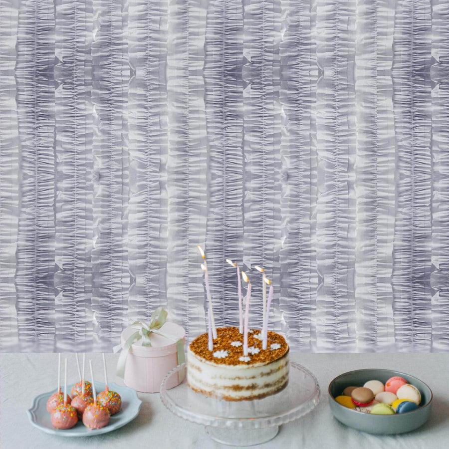 Decorative cake with candles and sweets on a table against textured wall backdrop.
