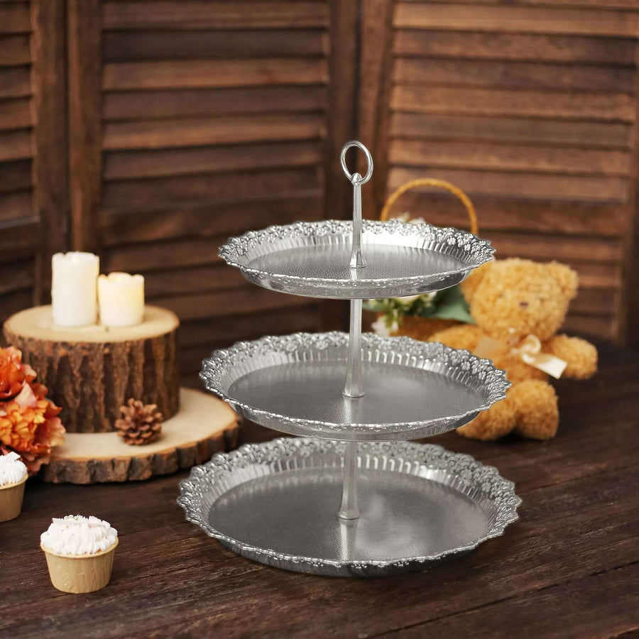 Three-tiered silver serving stand with decorative edges on a rustic wooden table.