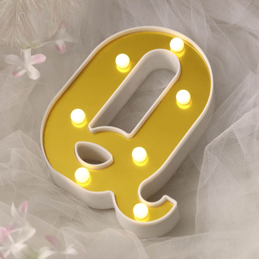 Yellow marquee letter "q" with lights on a soft background.