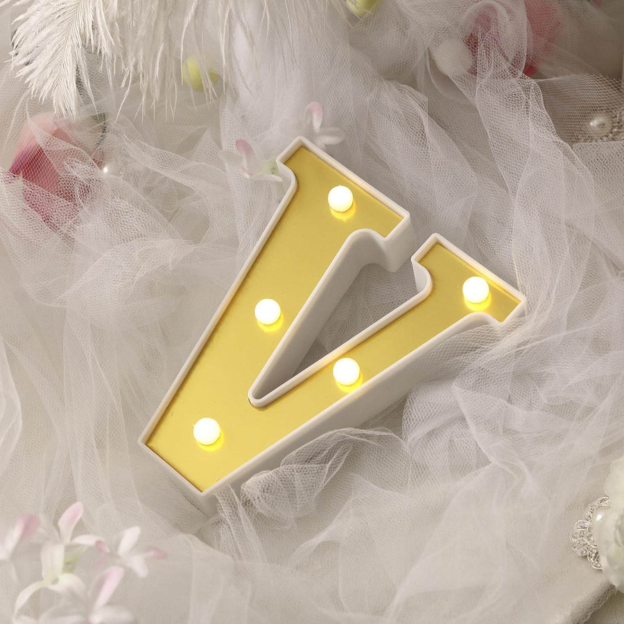 Decorative light-up letter "V" in yellow and white on soft fabric backdrop.