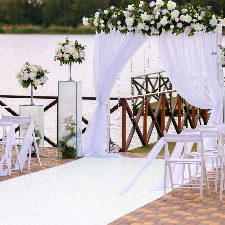 Elegant wedding setup with floral arch and white decor by the water.