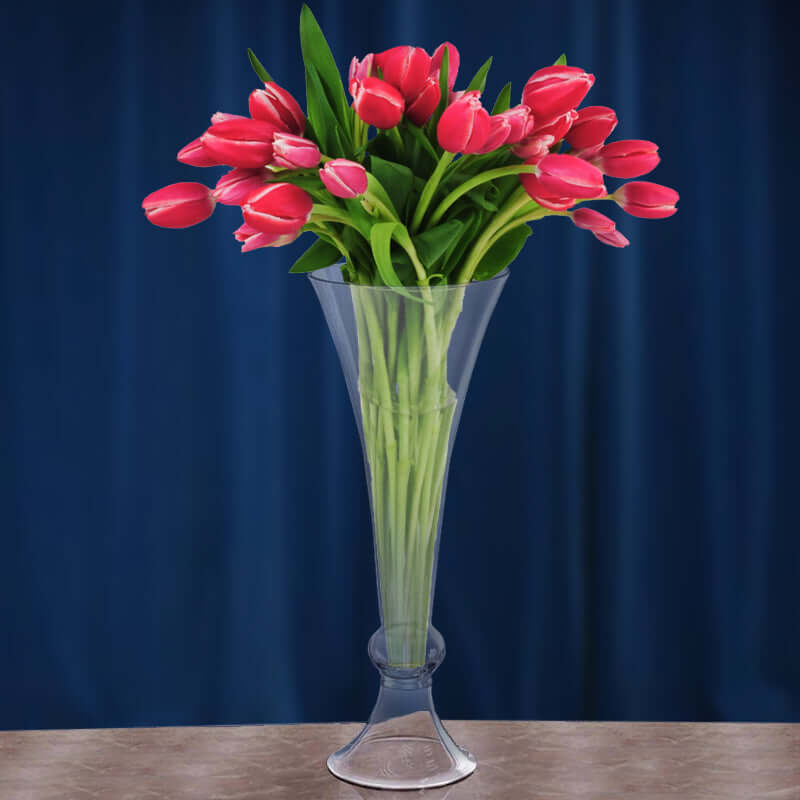 Clear vase with pink tulips against a blue backdrop.