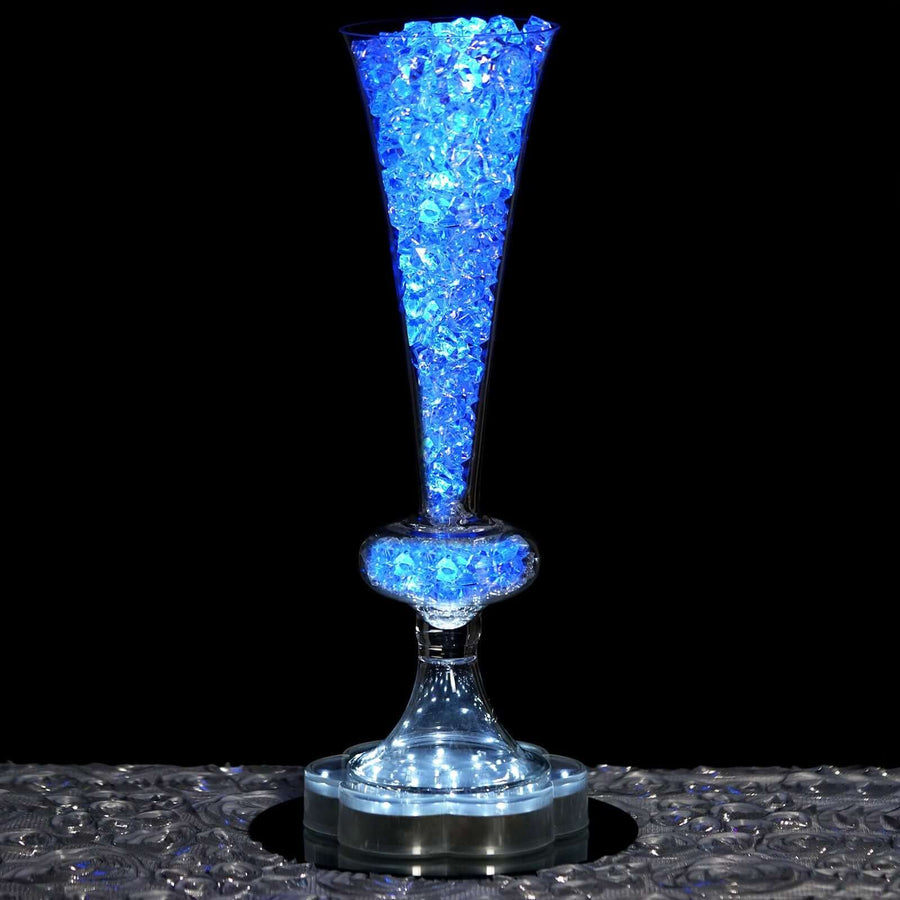 Illuminated glass vase filled with blue decorative stones against a dark background.