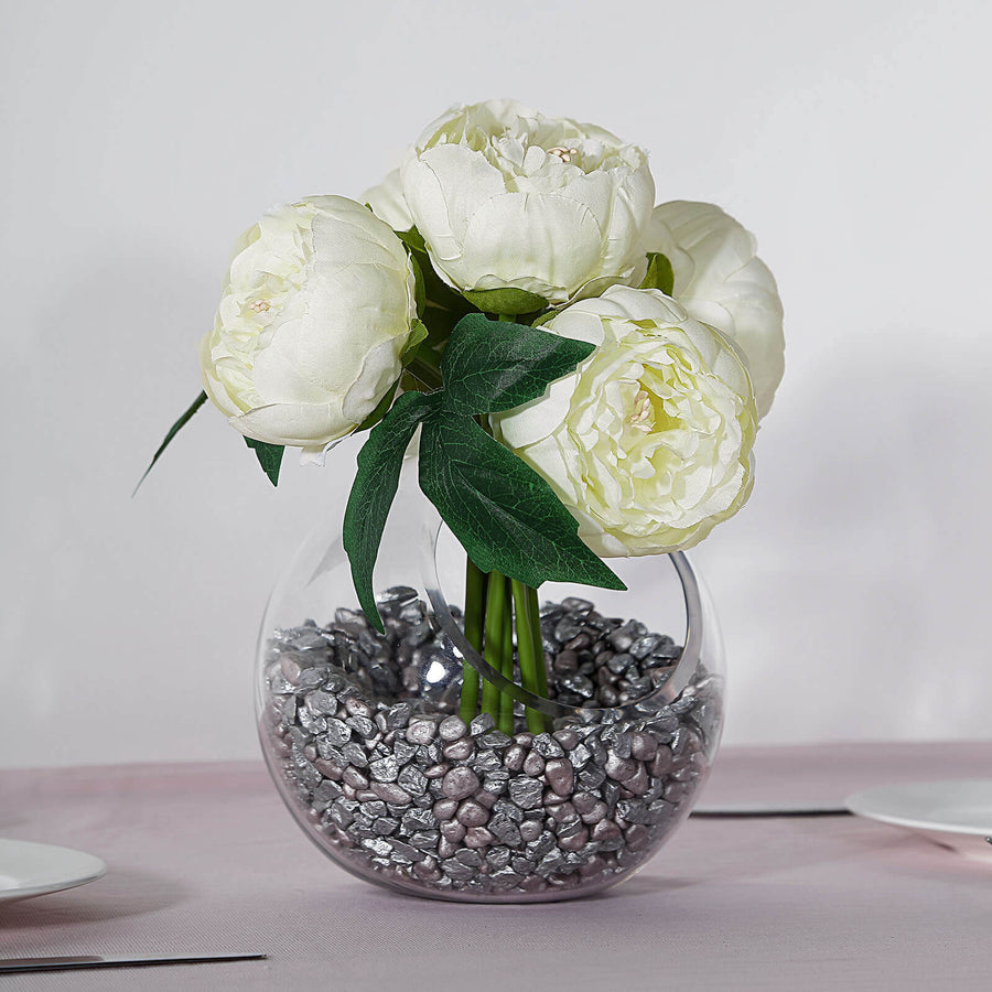 Artificial white peony bouquet in a glass vase with decorative stones.