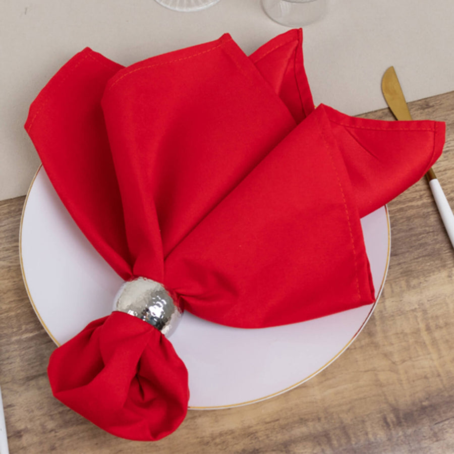 Red cloth napkin elegantly arranged on a plate with a silver napkin ring.