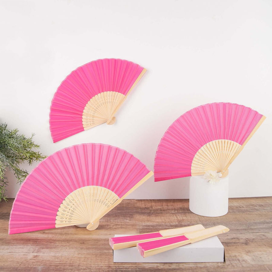 Pink decorative fans displayed on a wooden surface against a white backdrop.