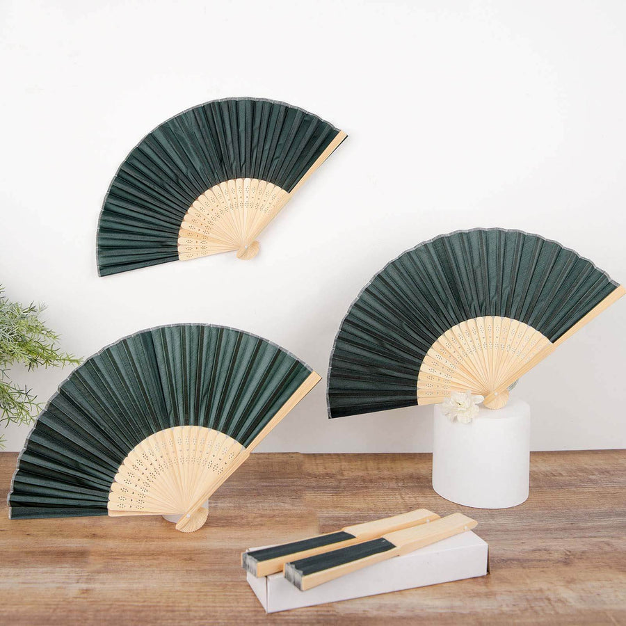 Three elegant green folding fans with wooden handles displayed on a rustic table.