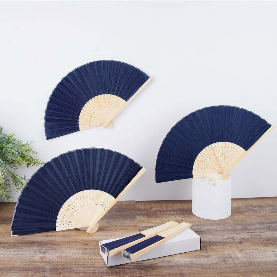 Navy folding fans displayed with a white vase and wooden surface.