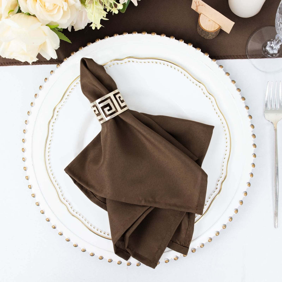 Brown napkin with decorative ring on an elegant dinner plate.