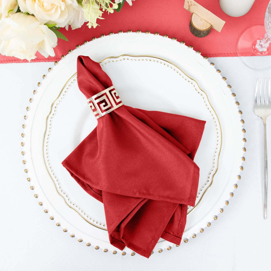 Elegant red napkin with decorative ring on a white plate, set for a dining occasion.