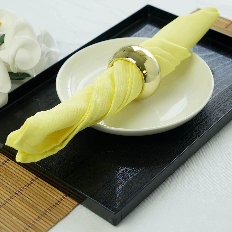 Yellow napkin with gold ring on a white plate in a black tray.