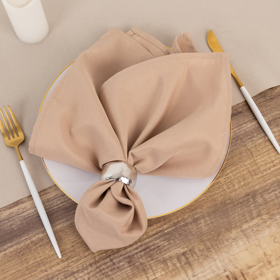 Beige cloth napkin elegantly wrapped with a silver napkin ring on a plate.