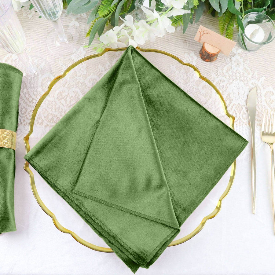 Green velvet napkin on elegant table setting with gold accents and floral decor.