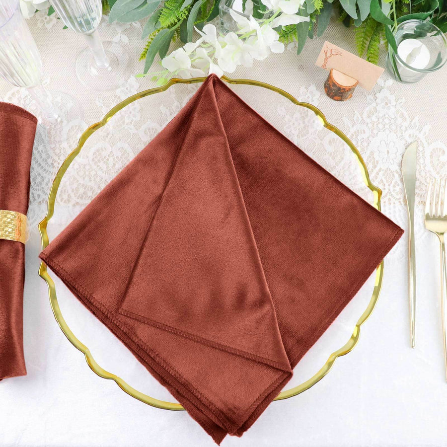 Brown cloth napkin elegantly displayed on a gold plate at a dining table.
