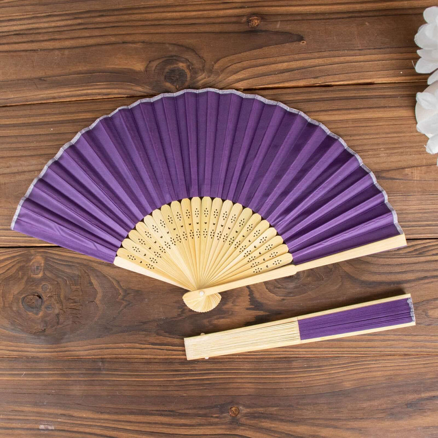 Purple folding fan with bamboo handle on wooden surface.