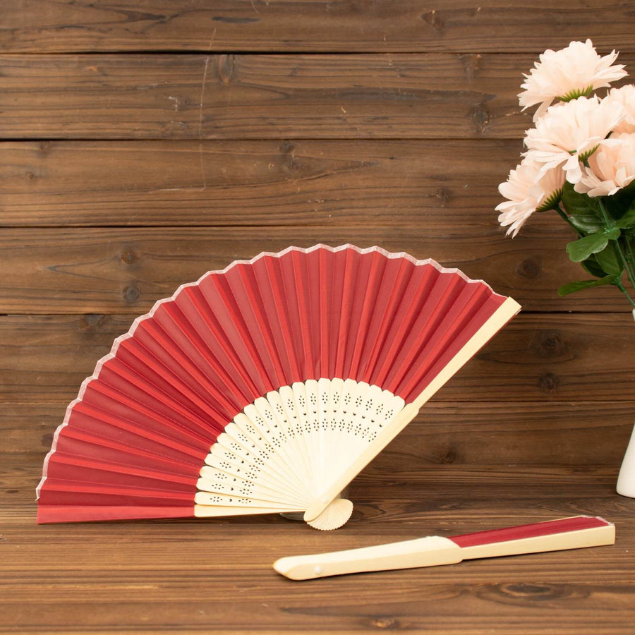 Red folding fan with cream details beside a vase of pink flowers.
