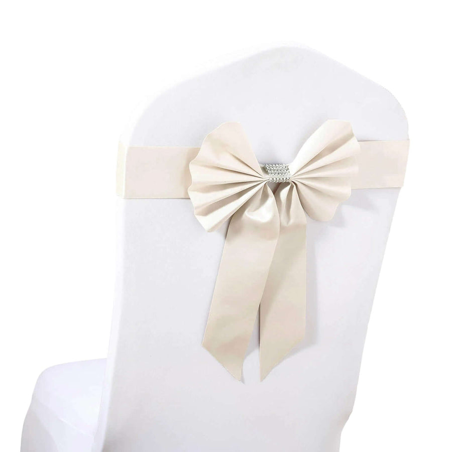 Beige satin chair sash with bow and rhinestone detail on white chair.