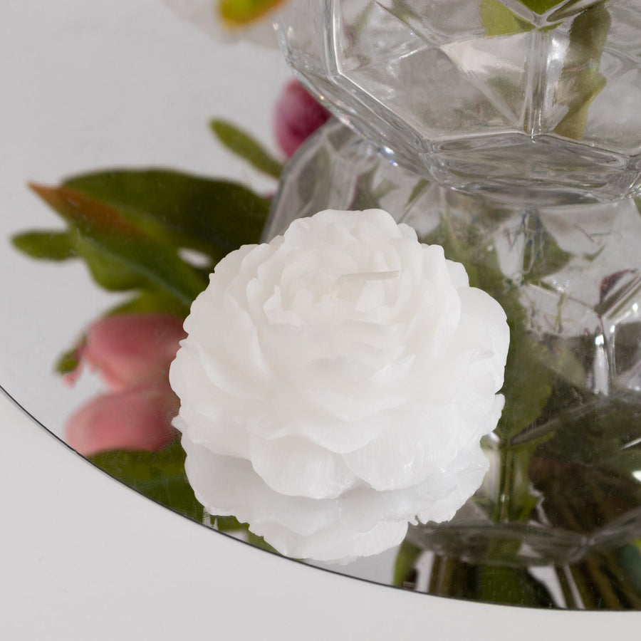 White floral candle on a mirror surface with reflections.