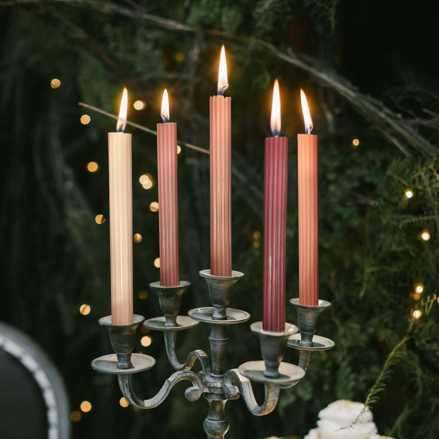 Elegant candlestick with five colorful tapered candles lit in a cozy setting.